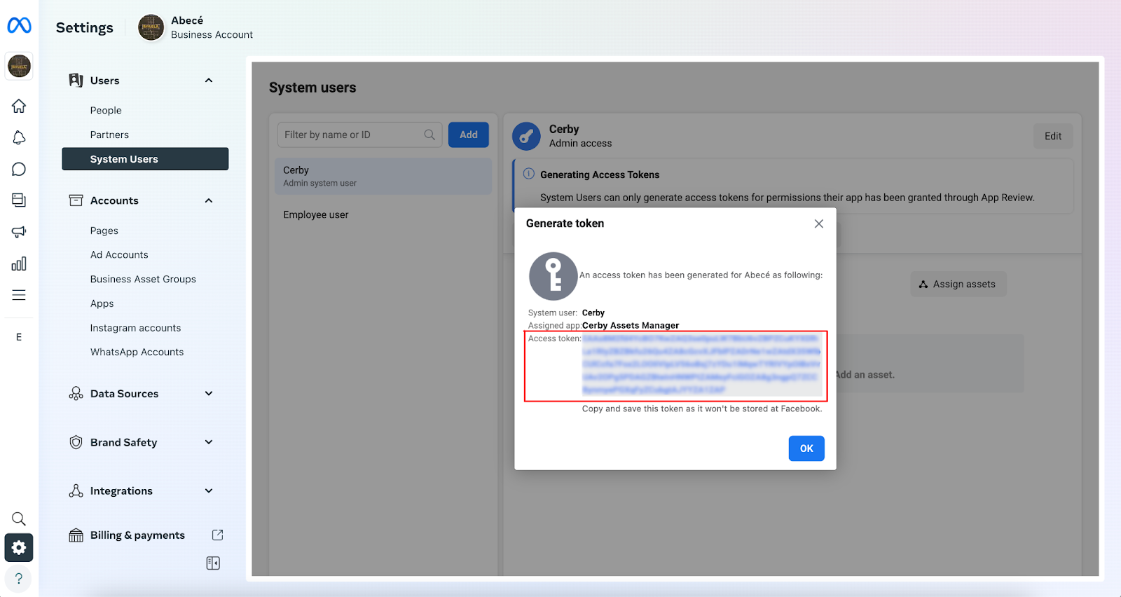 Screenshot of the Settings page of a Meta Business Manager. The Generate token dialog box is displayed on top of the System users page with an access token you can copy and an OK button.
